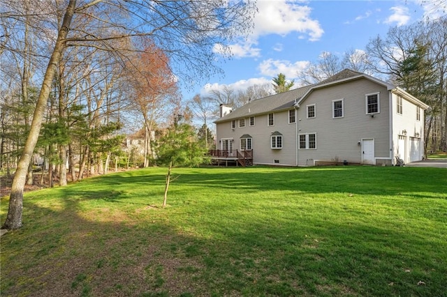 back of property featuring an attached garage, a wooden deck, a chimney, and a yard