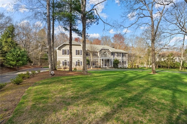 view of front facade featuring a front lawn, stone siding, a balcony, and driveway
