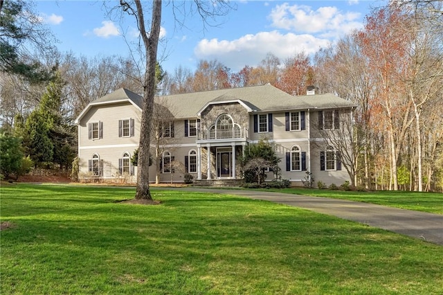 colonial-style house featuring a chimney, stone siding, a balcony, and a front yard