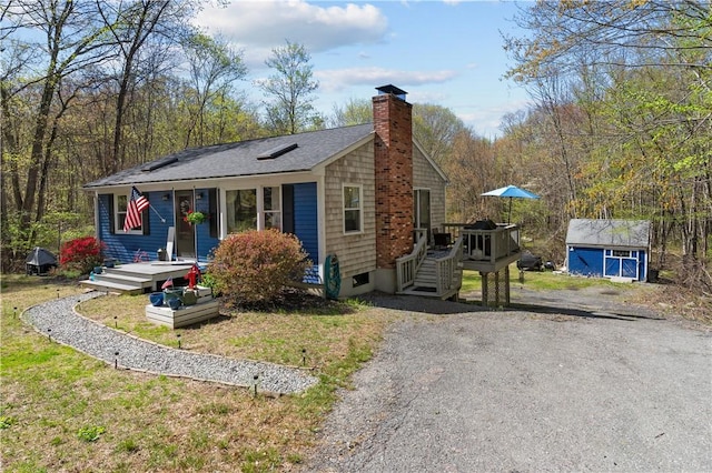 view of front of house featuring a chimney, an outbuilding, a deck, and a shingled roof
