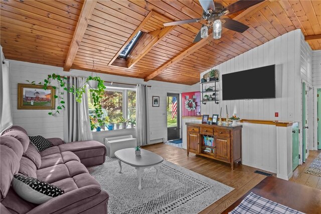 living area featuring a skylight, wood ceiling, wood walls, hardwood / wood-style flooring, and ceiling fan
