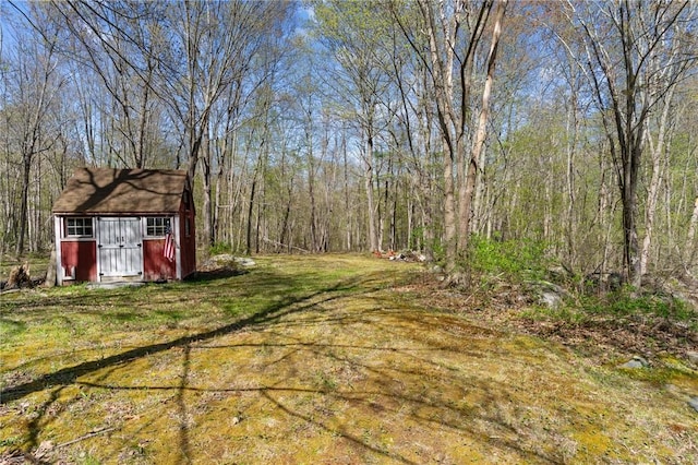 view of grassy yard with a shed, an outbuilding, and a view of trees