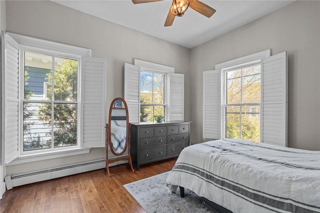 bedroom featuring multiple windows, a baseboard heating unit, and wood finished floors