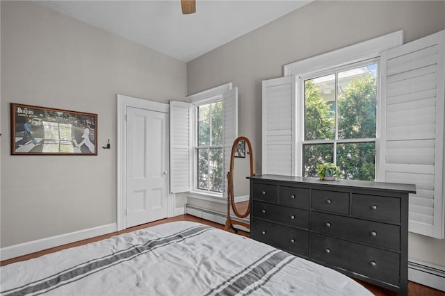 bedroom with a baseboard heating unit, baseboards, and wood finished floors
