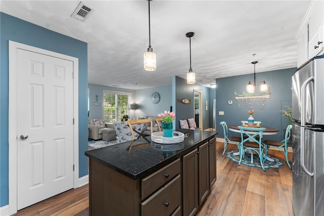 kitchen featuring dark brown cabinetry, visible vents, light wood-type flooring, freestanding refrigerator, and dark stone counters