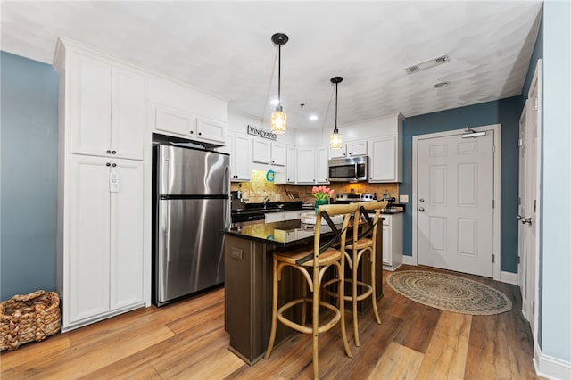 kitchen with a kitchen bar, visible vents, dark countertops, stainless steel appliances, and white cabinetry