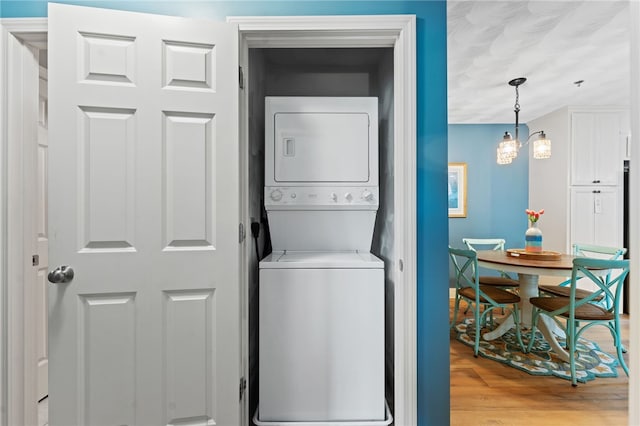 laundry room featuring laundry area, stacked washer and clothes dryer, light wood-style floors, and an inviting chandelier