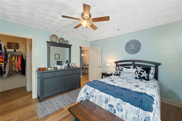 bedroom with ceiling fan, a spacious closet, wood finished floors, and a closet