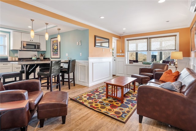 living room featuring a wainscoted wall, light wood finished floors, ornamental molding, a decorative wall, and recessed lighting