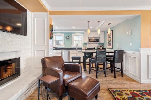 interior space featuring crown molding, wainscoting, a glass covered fireplace, a decorative wall, and light wood-style flooring