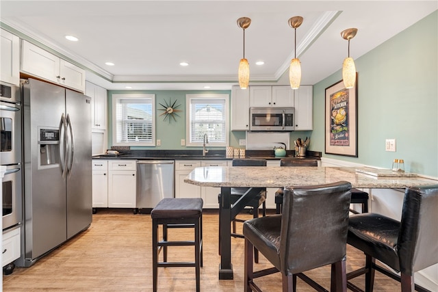 kitchen with a breakfast bar area, dark stone countertops, stainless steel appliances, light wood-type flooring, and ornamental molding