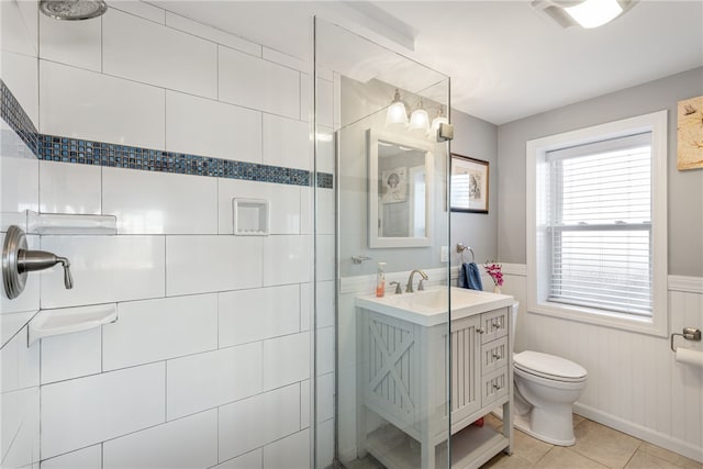 bathroom with tile patterned flooring, a wainscoted wall, vanity, toilet, and tiled shower