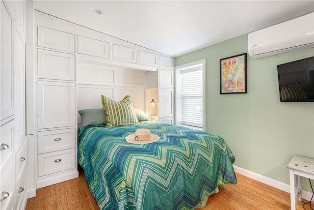 bedroom with baseboards, a wall mounted air conditioner, and light wood finished floors