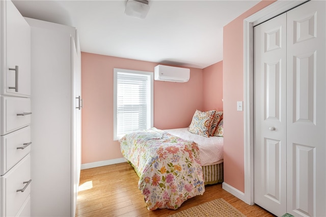 bedroom featuring an AC wall unit, baseboards, a closet, and light wood-style floors