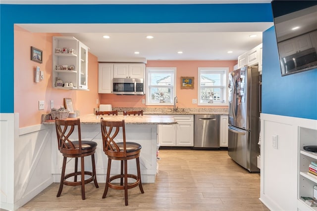kitchen with wainscoting, a sink, stainless steel appliances, white cabinetry, and a peninsula