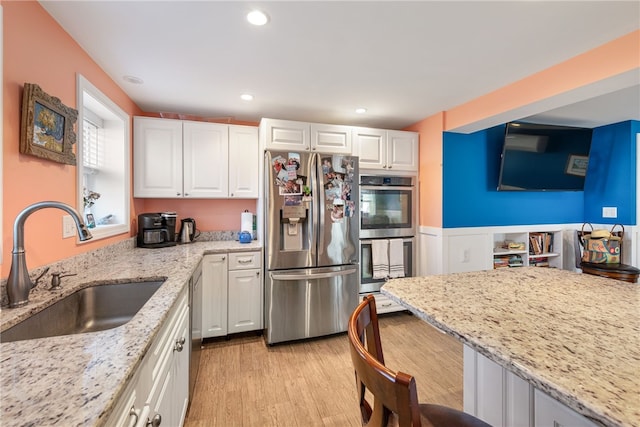 kitchen with white cabinetry, appliances with stainless steel finishes, a sink, and light stone counters