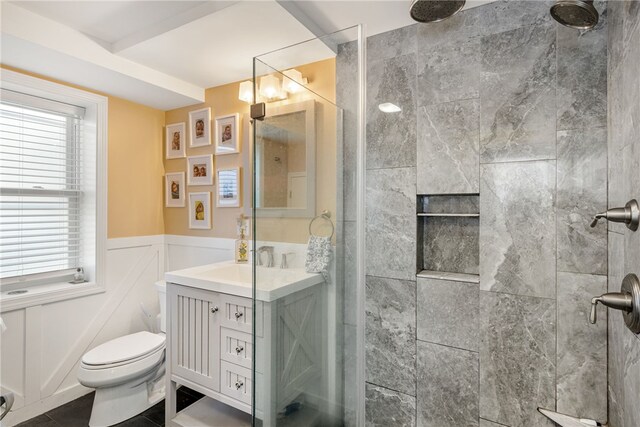 bathroom featuring vanity, a wainscoted wall, toilet, and tiled shower