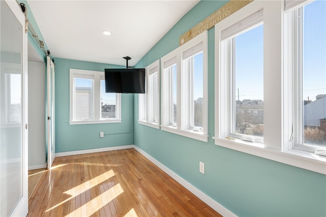 empty room featuring recessed lighting, baseboards, hardwood / wood-style flooring, and a barn door