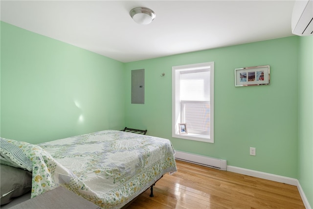 bedroom featuring light wood-style floors, baseboards, baseboard heating, a wall unit AC, and electric panel