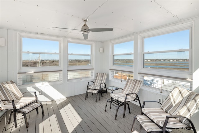sunroom with a ceiling fan, wood walls, wood finished floors, and a water view