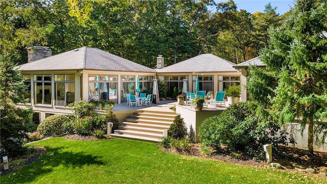 back of property with a yard, a chimney, a wooden deck, and a sunroom