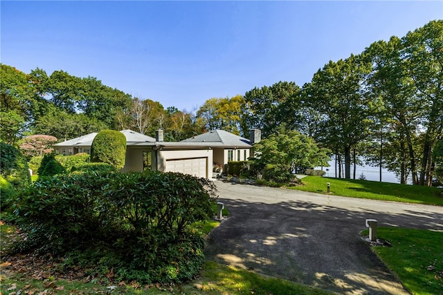 view of front facade with aphalt driveway, an attached garage, a front lawn, and a chimney