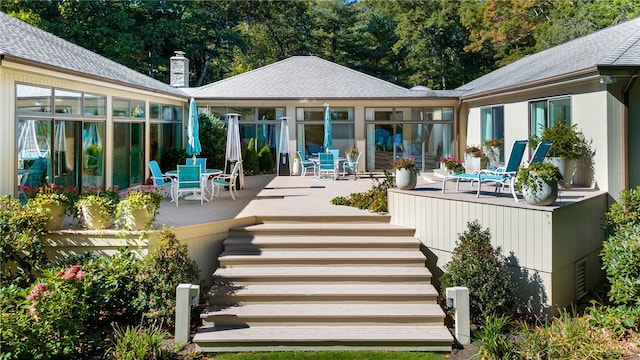 back of property featuring stairway, a chimney, a wooden deck, and outdoor dining space