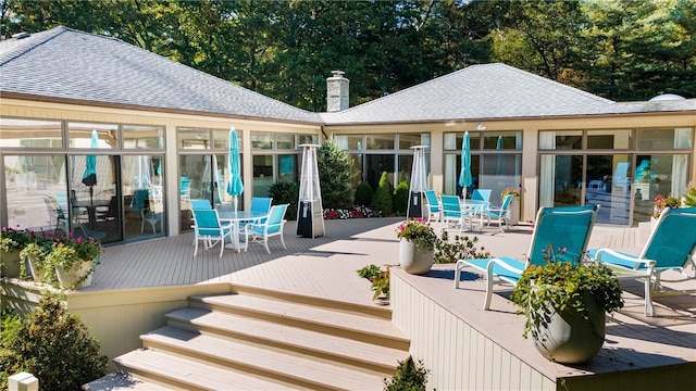 exterior space featuring a chimney, a deck, outdoor dining space, and a shingled roof
