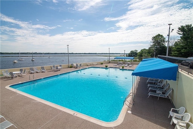 community pool with a patio area, a water view, and fence