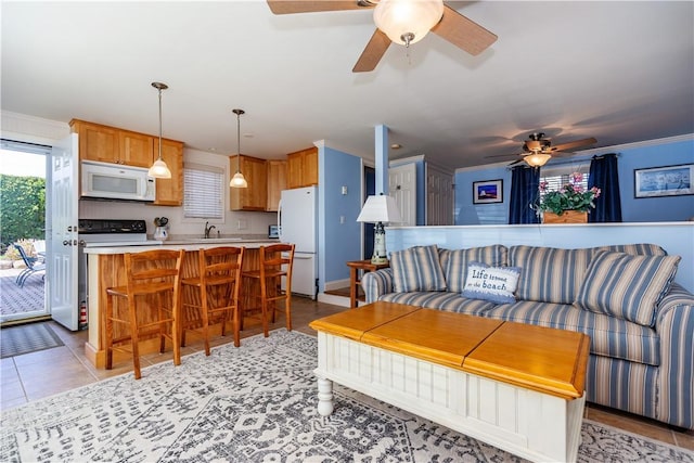 living area with a ceiling fan, ornamental molding, and light tile patterned flooring