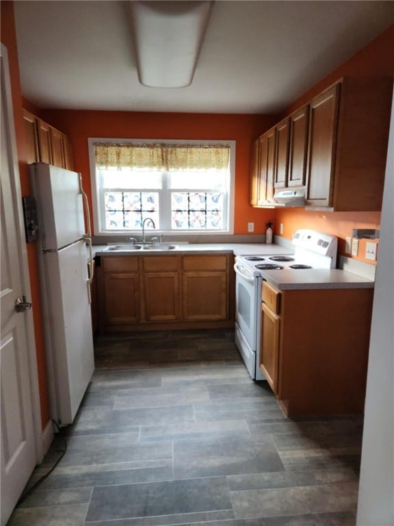 kitchen with brown cabinets, a sink, white appliances, under cabinet range hood, and light countertops