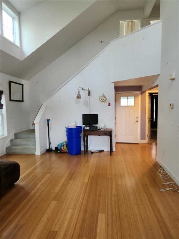 living area with stairway, light wood finished floors, and high vaulted ceiling