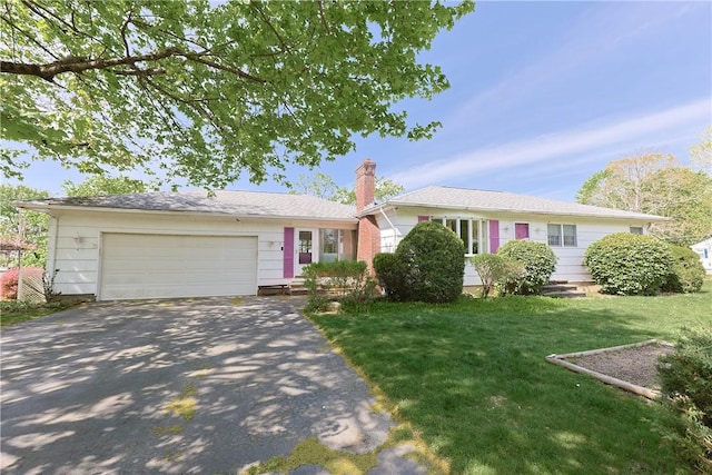 ranch-style house featuring an attached garage, a chimney, a front yard, and aphalt driveway