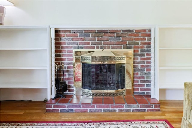 details with built in shelves, a brick fireplace, and wood finished floors