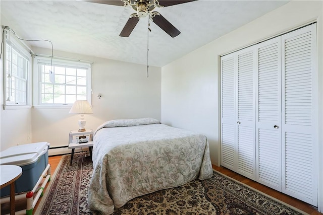 bedroom with a closet, wood finished floors, baseboard heating, and ceiling fan