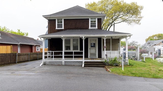 view of front of house with a porch, roof with shingles, a front lawn, and fence