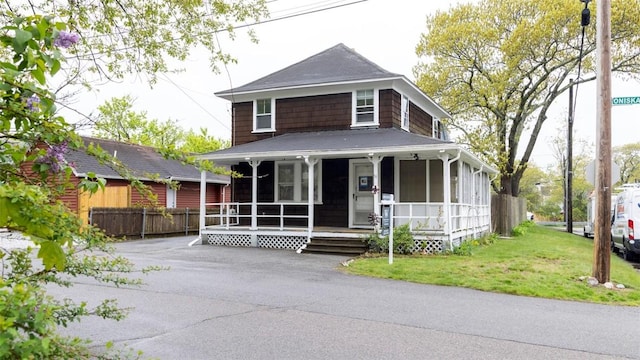 farmhouse featuring a front yard, covered porch, and fence