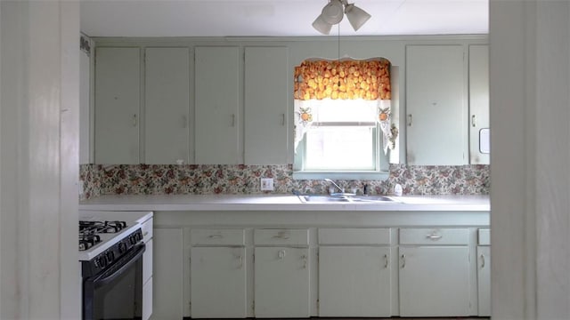 kitchen featuring a ceiling fan, gas range, light countertops, and a sink