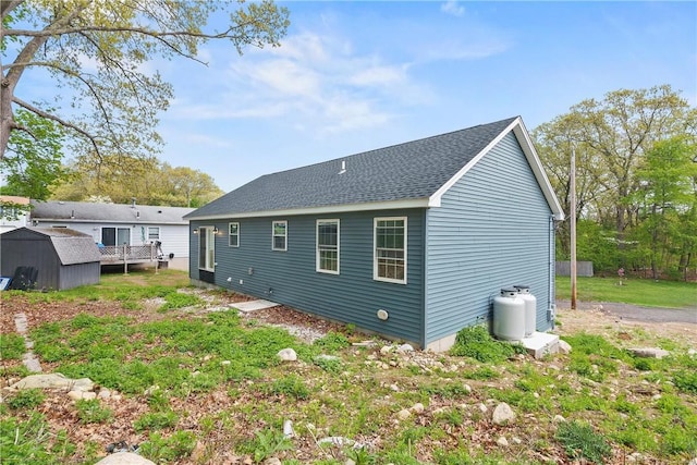 back of property featuring a storage shed, a shingled roof, and an outbuilding
