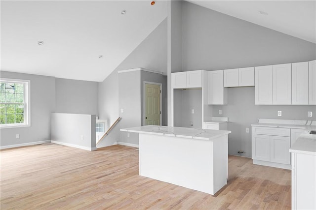 kitchen with baseboards, high vaulted ceiling, a kitchen island, light wood-style floors, and white cabinets