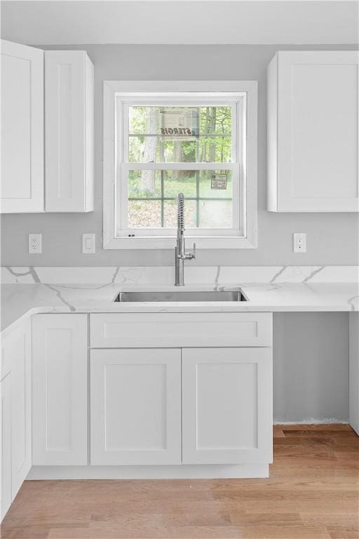 kitchen featuring white cabinetry, light stone counters, light wood-type flooring, and a sink