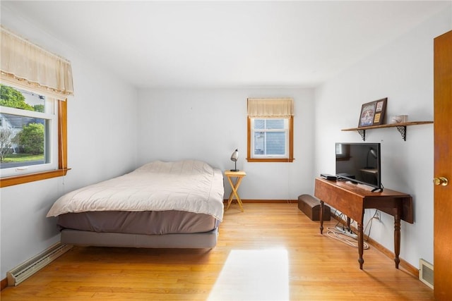 bedroom featuring a baseboard radiator, baseboards, light wood-type flooring, and visible vents