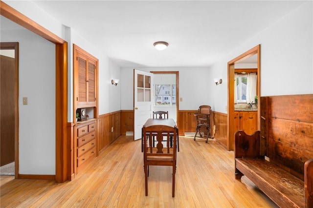 dining space with wainscoting, light wood-style flooring, and wooden walls