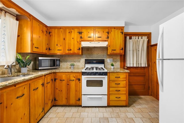 kitchen featuring under cabinet range hood, decorative backsplash, a sink, and white appliances