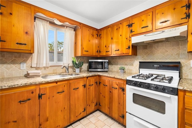 kitchen with under cabinet range hood, white gas range, a sink, stainless steel microwave, and brown cabinets