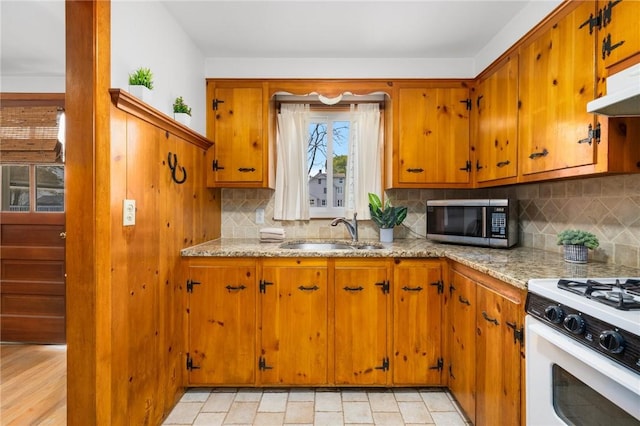 kitchen featuring brown cabinets, white range with gas cooktop, a sink, and stainless steel microwave