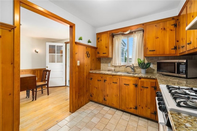 kitchen featuring brown cabinetry, white gas range oven, a sink, and stainless steel microwave