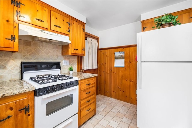 kitchen with brown cabinetry, white appliances, tasteful backsplash, and under cabinet range hood