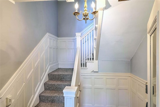 stairs featuring a chandelier, carpet flooring, a decorative wall, and a wainscoted wall