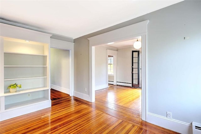 spare room featuring baseboards, baseboard heating, built in shelves, a baseboard radiator, and hardwood / wood-style flooring